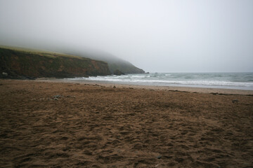 St Michael Caerhays beach on a wet overcast day, seaweed covered rocks visible above smooth sand