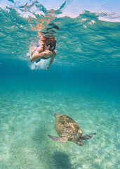 Snorkelling in Marsa Mubarak, Egypt, young woman swimming above green sea turtle, showing thumb up