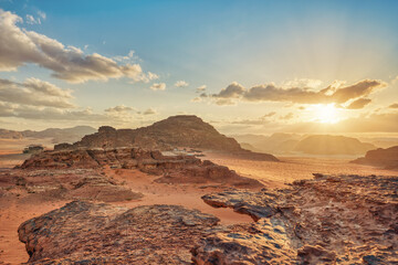 Morning at Wadi Rum desert, sun rising above rocky mountains terrain in distance, camp tents...