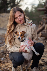 Young woman crouching, holding her Jack Russell dog which looks curious