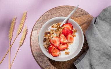 Granola or muesli with natural greek yogurt, strawberry in a bowl on a wooden board on a violet...