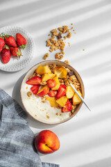 Granola or muesli with natural greek yogurt, strawberry and peach in a bowl on a white background