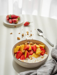 Granola or muesli with natural greek yogurt, strawberry and peach in a bowl on a white table near...