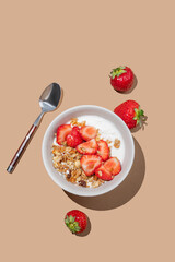 Granola or muesli with natural greek yogurt and strawberry in a bowl on a bright beige background