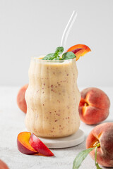Smoothie with peach and banana in a glass on a marble stand on a light background with tropical...