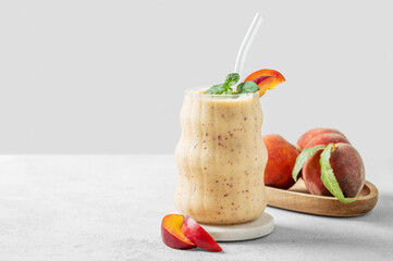 Smoothie with peach and banana in a glass on a marble stand on a light background with tropical...