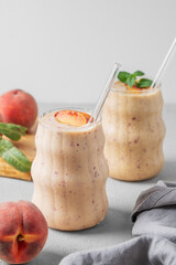 Two glasses of smoothie with peach and banana on a light background with tropical fruits and napkin.