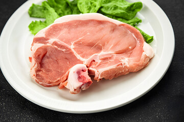 Fresh raw pork chop on white plate with green lettuce ready for cooking and meat preparation in kitchen