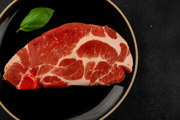 Raw pork steak on black plate with fresh basil leaf ready for cooking and gourmet meal preparation