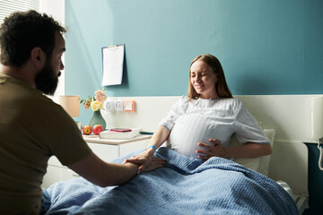 Caucasian pregnant young adult woman experiencing labor pain lying in hospital bed holding stomach...