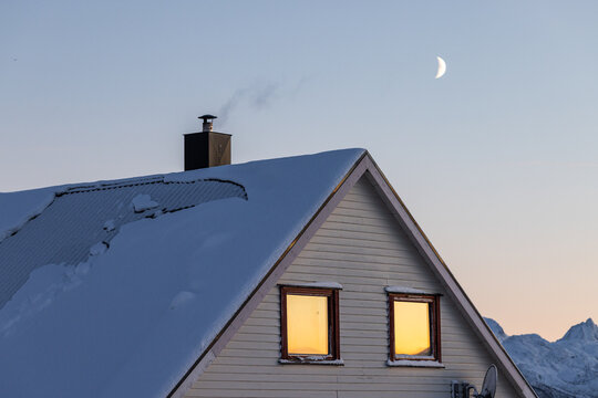 Fototapeta Snow-covered house roof with glowing windows and crescent moon