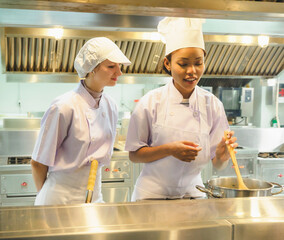 Professional female two chefs tasting food in culinary training education modern kitchen wearing...