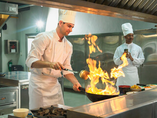 Chefs professional action demonstrating their stand cooking skills over high flame in commercial kitchen. Image shows culinary expertise and energetic and passionate atmosphere of the culinary arts.