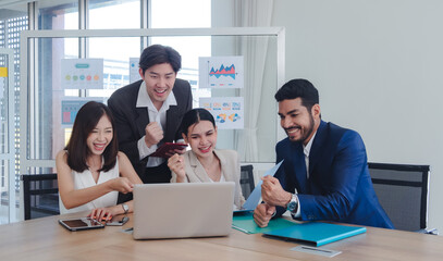 Group business professional celebrate in office around table laptop tablet document spread individual dressed formal attire appear excited success. background  chart/graph wall indicate performance.