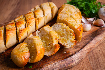 garlic bread,baguette with garlic butter and herbs, on a wooden board, with herbs and garlic cloves,