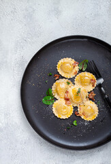 fresh ravioli, with butter, spices and herbs, fried bacon, on a black plate, top view, dark background, no people,