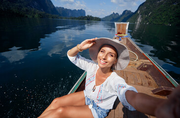 Travel selfie photo featuring a happy woman on a boat in a picturesque lake, enjoying vibrant...