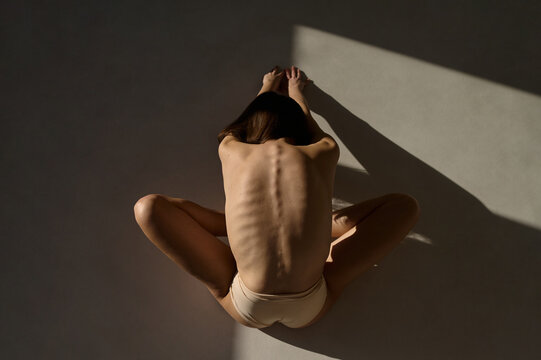 skinny woman in underwear sitting on a white background on a sun ray