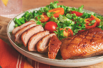 Delicious grilled duck breast served with fresh garden salad and cherry tomatoes at a rustic dining table