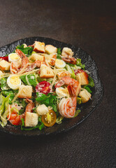 caesar salad with tiger prawns, shrimp salad, lettuce leaves, quail eggs, cherry tomatoes, parmesan cheese, on a black plate,