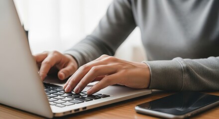 Hands typing on a laptop computer with a smartphone nearby