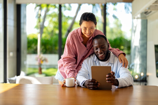 Young happy multiethnic couple having fun while using tablet at home. Happy couple discussing future - Powered by Adobe