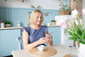 Senior woman at her kitchen drinking coffee and checking messages on her mobile phone