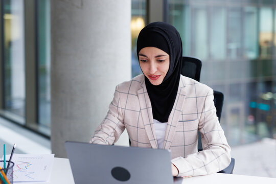 Muslim customer support specialist typing message to client on laptop