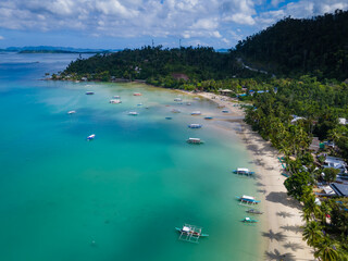 Port Barton beach with many traditional Filipino boats on the coastline. Aerial drone view of sandy beach with tropical palms. Palawan, Philippines