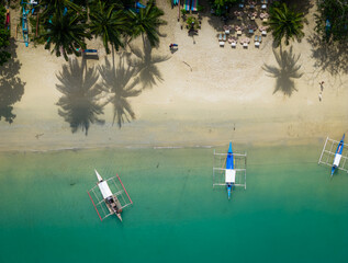 Port Barton beach with many traditional Filipino boats on the coastline. Aerial drone view of sandy beach with tropical palms. Palawan, Philippines