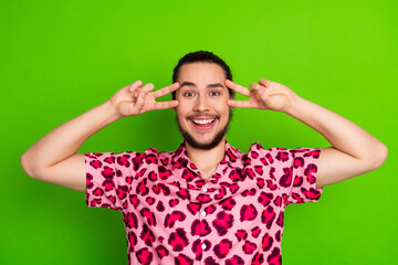 Cheerful man wearing pink leopard print shirt making a playful gesture standing against a vibrant...