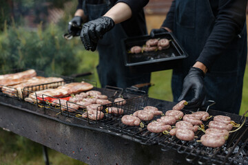 Hands preparing sausages on charcoal grill