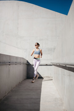 Woman running in modern architectural pathway under bright blue sky