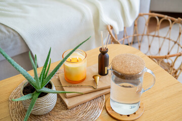 Homely atmosphere. Carafe of water, an aloe houseplant, an aroma diffuser, and a candle on a coffee table in the living room.