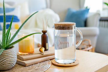 Homely atmosphere. Carafe of water, an aloe houseplant, an aroma diffuser, and a candle on a coffee table in the living room.