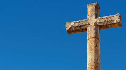 Weathered stone cross stands tall against clear blue sky, symbolizing faith and resilience. texture of stone adds character, creating serene and uplifting atmosphere