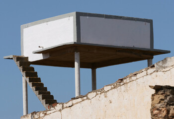 Dilapidated abandoned building complex, elevated water tank standing on a concrete platform with...