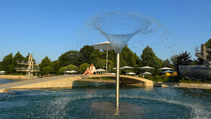 Swimming pool with unique fountain and young woman sitting on bridge, outdoor public recreation...