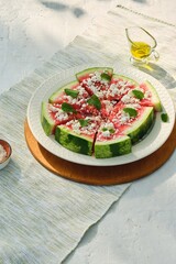 Appetizer, watermelon chunks with rind, sprinkled with crumbled feta cheese, drizzled with olive oil and garnished with mint leaves on a ceramic plate.