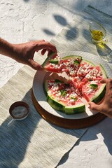 Appetizer, watermelon chunks with rind, sprinkled with crumbled feta cheese, drizzled with olive oil and garnished with mint leaves on a ceramic plate.