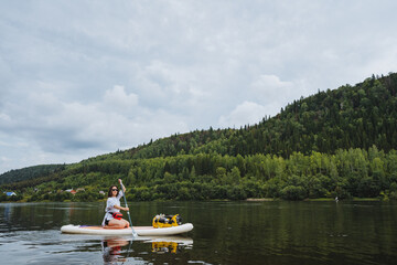 Two individuals enjoy paddleboarding on a calm lake, surrounded by lush greenery and dramatic...