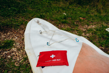 A bright red first aid kit is placed on a clean white surface outdoors, filled with a variety of essential supplies such as bandages and safety pins, ensuring safety during various outdoor activities