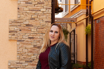Photo shoot of a blonde woman in a black leather jacket and a burgundy sweater in the center of the...