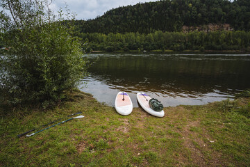 A serene riverside view features colorful paddleboards on a sandy shore, surrounded by lush greenery and calm waters, offering a perfect backdrop for adventures or peaceful relaxation in nature