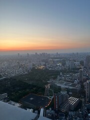 Tokyo skyline at dusk with Shinjuku skyscrapers glowing under a vibrant sunset sky, city lights beginning to twinkle over Japan’s bustling urban landscape