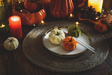Thanksgiving table setting with decorative pumpkins, candles and string lights on dark wooden table