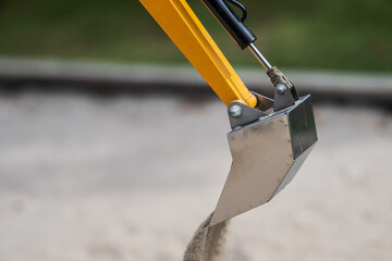 Closeup of metallic sandbox digger arm in motion.
