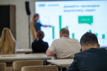 Group of people attentively watching presentation in office setting featuring charts and graphs