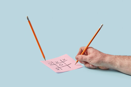 Hand playing tic tac toe with pencil on blue background