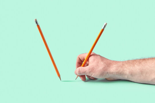 Hand using pencil beside upright pencil on green surface